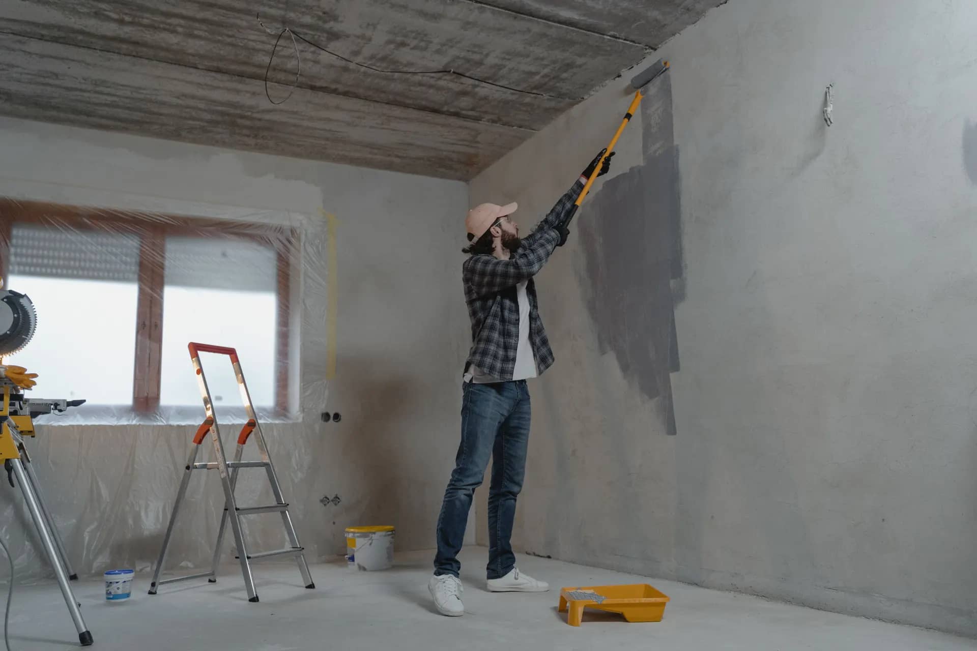 Decorator rolling grey paint onto a wall in a room under renovation