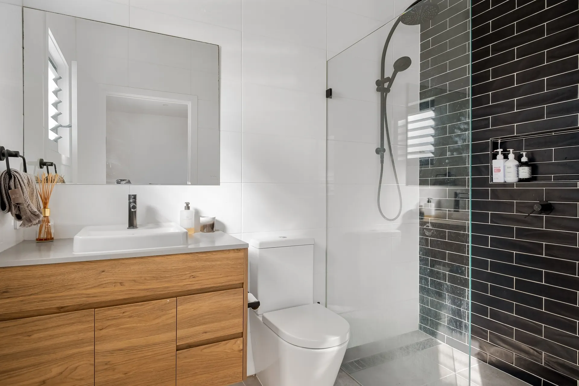 Renovated bathroom with a glass walk-in shower, timber vanity and dark wall tiles
